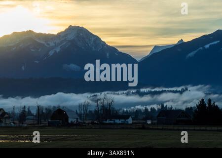 Une vue à couper le souffle avec des montagnes enneigées qui brillent dans la lumière tôt le matin avec du brouillard dérivant sur la vallée, complétée par une atmosphère sereine Banque D'Images