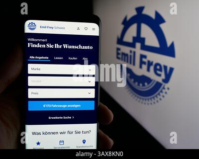 Dans cette illustration photo, une personne tient un téléphone portable avec la page web de la société automobile suisse Emil Frey Holding AG sur l'écran devant le logo. Banque D'Images