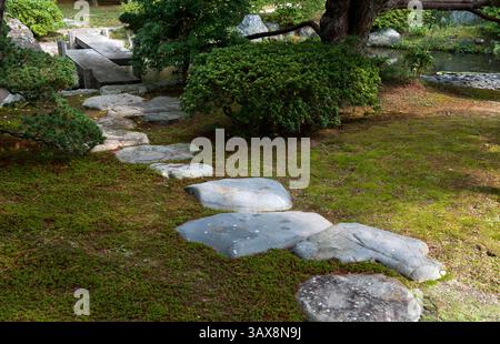 Sentier de pierre d'escalier à travers le jardin de mousse menant à un pont de planches en pierre zigzag à Oikeniwa au jardin paysager du Palais impérial de Gosho, Kyoto, Japon. Banque D'Images
