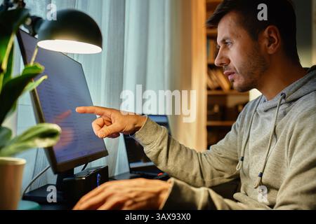 Homme assis au bureau dans le salon et utilisant l'ordinateur pour le travail à distance. Homme freelance travaillant au bureau à domicile Banque D'Images