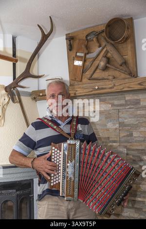L'homme joue de l'accordéon traditionnel de Styrie dans le salon de la ferme Banque D'Images