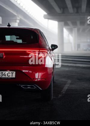 Red SEAT Leon sous un pont le matin brumeux. Vue arrière rapprochée du côté droit du hayon rouge, deux ponts en arrière-plan recouverts d'un épais brouillard. Banque D'Images
