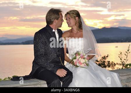 Mariée et mariée assis devant un lac au coucher du soleil Banque D'Images
