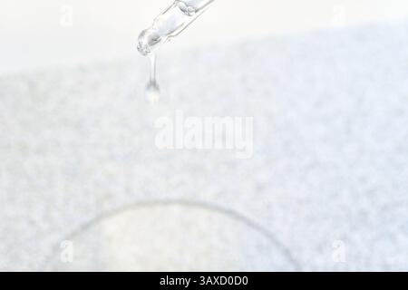 Gros plan d'une gouttelette de liquide provenant d'un compte-gouttes en verre sur un arrière-plan flou. Banque D'Images