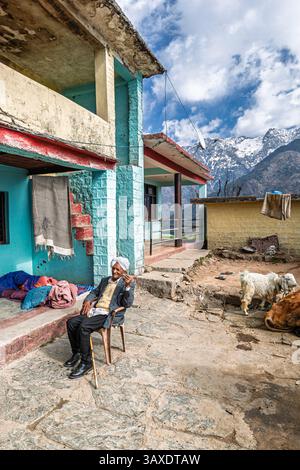 Un homme âgé du coin portant un turban blanc fume dans une cour de ferme du village à Naddi View point, célèbre pour ses vues sur la chaîne de Dhauladhar Banque D'Images