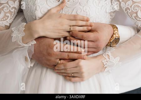 Mains tenant ensemble avec des anneaux de mariage ; un gros plan des mains entrelacées d'un couple affichant des anneaux de mariage dorés sur des manches en dentelle blanche. Banque D'Images