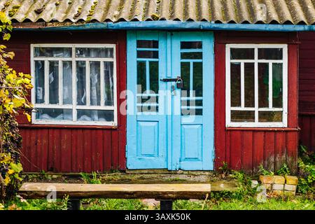 Porte en bois bleu clair et fenêtres blanches d'une petite maison rouge avec toit en ardoise Banque D'Images