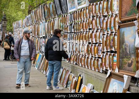 Londres, Royaume-Uni. 20 avril 2025. Un touriste regarde de plus près la peinture encadrée sur le côté nord de Hyde Park. Une très grande sélection de peintures attendent d'être épuisées sur le côté nord de Hyde Park près de Piccadilly à Londres, Royaume-Uni. C'est un endroit très populaire pour acheter une peinture entre les touristes et les habitants. Crédit : SOPA images Limited/Alamy Live News Banque D'Images