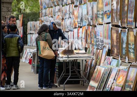 Londres, Royaume-Uni. 20 avril 2025. Un couple regarde de plus près les impressions sur toile du côté nord de Hyde Park. Une très grande sélection de peintures attendent d'être épuisées sur le côté nord de Hyde Park près de Piccadilly à Londres, Royaume-Uni. C'est un endroit très populaire pour acheter une peinture entre les touristes et les habitants. Crédit : SOPA images Limited/Alamy Live News Banque D'Images