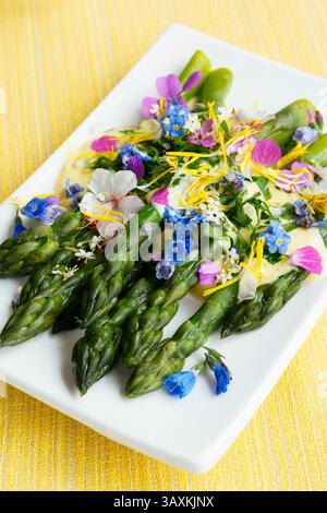 Asperges vertes avec une sauce safran et des fleurs comestibles servies dans une assiette. Banque D'Images