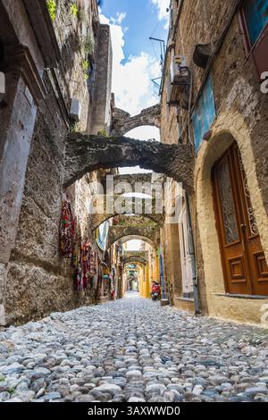 Une vue en angle bas le long d'une rue étroite typique dans la vieille ville de Rhodes, Grèce photographiée le 7 avril 2025 alors que de petits cailloux sont emballés étroitement dans le Banque D'Images