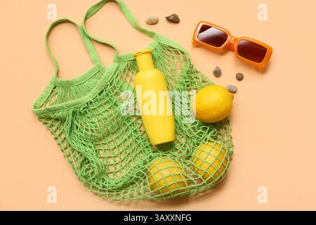Bouteille de crème solaire, lunettes de soleil et sac à ficelle avec des citrons sur fond orange Banque D'Images