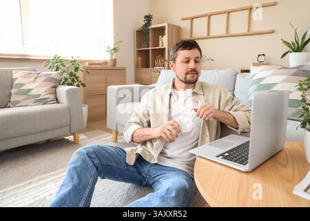 Jeune homme avec ordinateur portable ouvrant bouteille d'eau à la maison Banque D'Images