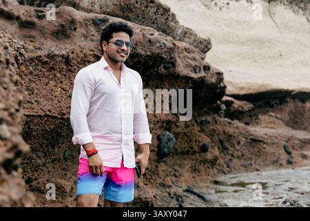 Souriant confiant homme indien élégant portant des lunettes de soleil à la plage relaxant. Banque D'Images