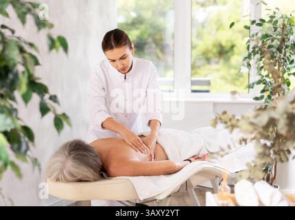 Femme âgée méconnaissable se couche face cachée sur le canapé et profiter de soins spa, massage des épaules Banque D'Images