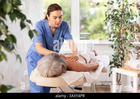 Femme âgée méconnaissable se couche face cachée sur le canapé et profiter de soins spa, massage des épaules Banque D'Images