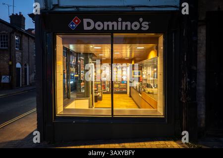 L'intérieur lumineux d'une pizzeria Domino's, visible à travers les fenêtres en verre la nuit à Saffron Walden. Banque D'Images