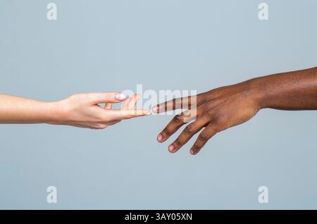 Femme caucasienne et homme africain se touchent le doigt l'un à l'autre sur fond gris. Concept de racisme. Deux mains doucement étirées désirant toucher viennent pendant Banque D'Images