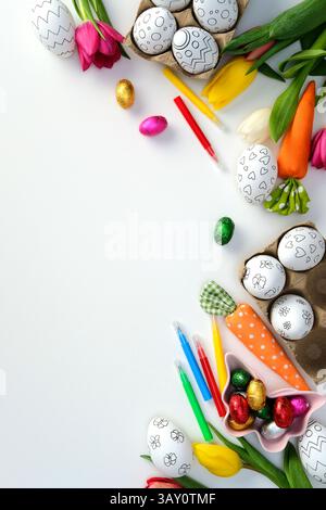 Oeufs de Pâques pour la coloration, stylos à pointe feutre, tulipes et décorations festives sur fond blanc. Plat, vue de dessus. Banque D'Images