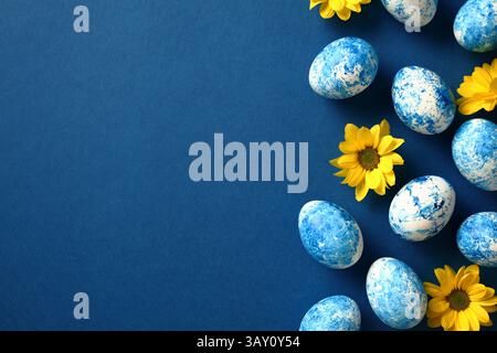 Fond bleu foncé avec des œufs de Pâques et des fleurs jaunes, espace de copie pour le texte et les salutations Banque D'Images