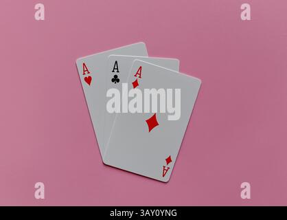 Trois cartes à jouer, tous as, disposées sur un fond rose doux. Chaque carte affiche une couleur différente : coeurs, clubs et diamants. Banque D'Images