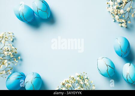 Œufs de Pâques bleus et en marbre avec des fleurs sur fond bleu pastel. Vue de dessus, pose à plat, espace de copie. Banque D'Images