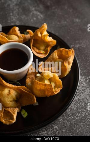 Wontons frits croustillants servis sur assiette noire avec sauce soja et oignons verts Banque D'Images