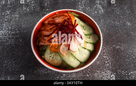Bol de salade de légumes frais avec concombres tranchés, tomates, betteraves râpées et carottes râpées, offrant un repas sain et vibrant Banque D'Images
