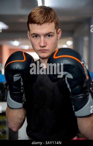 Jeune boxeur portant des gants de boxe posant dans un ring de boxe, prêt pour un sparring ou une séance d'entraînement Banque D'Images