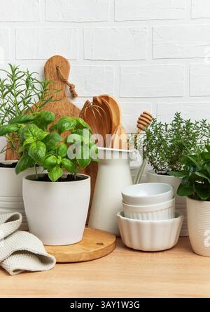 Les herbes aromatiques prospèrent dans les pots aux côtés des ustensiles de cuisine et de la vaisselle blanche, incarnant une atmosphère de cuisine confortable contre un mur de briques blanches Banque D'Images