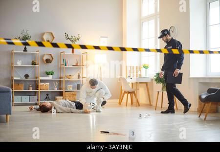 Expert médico-légal recueillant des preuves avec un officier de police inspectant la scène de crime avec un cadavre Banque D'Images