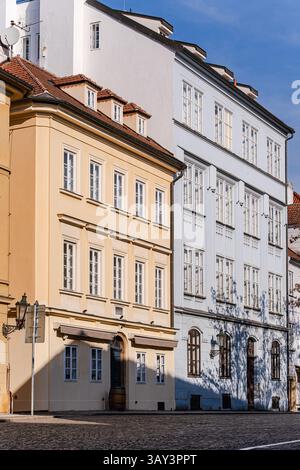 Bâtiments européens ensoleillés à l'architecture traditionnelle dans une rue pavée calme de Prague. Ciel bleu et ombres douces ajoutent au charme et à l'elega Banque D'Images