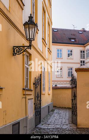 Ruelle pittoresque flanquée de bâtiments jaunes à Prague, avec une lanterne ornée et une porte en fer forgé. Chemin pavé ajoute du charme vintage au p Banque D'Images