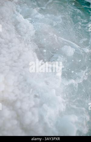 Gros plan capturant les formations salines texturées et les eaux bouillonnantes de la mer morte en Jordanie. Les teintes bleues et blanches naturelles créent une atmosphère sereine Banque D'Images