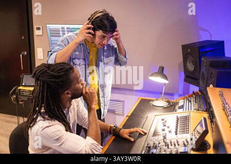 Deux hommes collaborent dans un studio d'enregistrement professionnel, entouré d'équipements audio et de moniteurs, créant de la musique avec la technologie moderne et concentré Banque D'Images