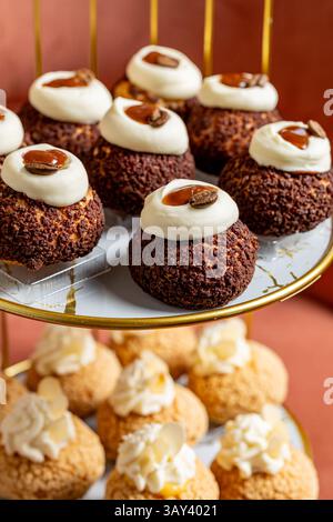 Un assortiment tentant de pâtisseries à choux se dresse élégamment sur un stand doré. Recouvertes de glaçage crémeux et de garnitures, ces délicieuses friandises sont parfaites Banque D'Images