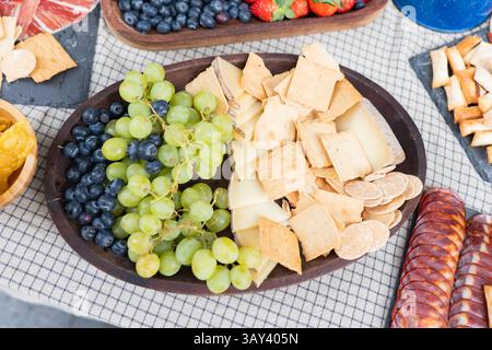 Un tableau de charcuterie appétissant composé de raisins verts et noirs, de tranches de fromage assorties et d'un éventail de craquelins croustillants, parfait pour un rafraîchissement Banque D'Images