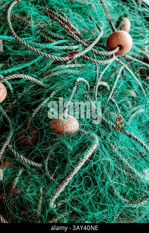 Gros plan d'un filet de pêche affichant des textures et des motifs complexes. Le filet a de la ficelle verte et est enchevêtré avec des cordes. Les bouées en bois ajoutent du contraste et Banque D'Images
