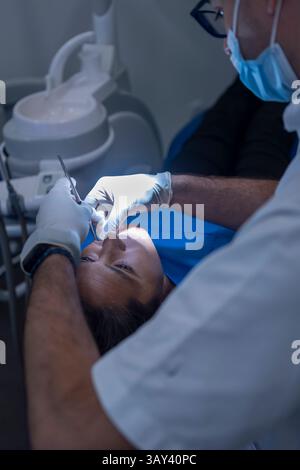 Dentiste en équipement de protection effectuant le nettoyage des dents d'un patient à l'aide d'outils dentaires. L'accent est mis sur la santé bucco-dentaire, mettant en évidence les soins dentaires de routine dans Banque D'Images