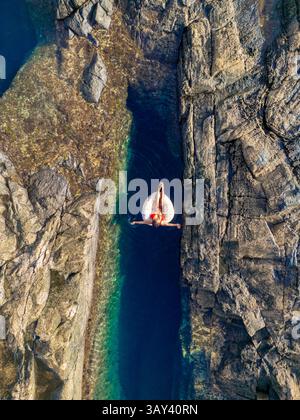 Vue de dessus d'une femme méconnaissable se relaxant sur un flotteur gonflable dans une piscine naturelle sereine et étroite entourée de falaises accidentées à Tindaya Beach, Fue Banque D'Images