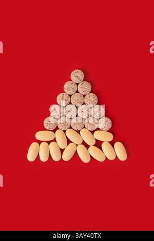 Collection de capsules et de pilules organisées dans un arbre de Noël comme la formation sur un fond rouge vif, symbolisant la santé et les médicaments pendant la Banque D'Images