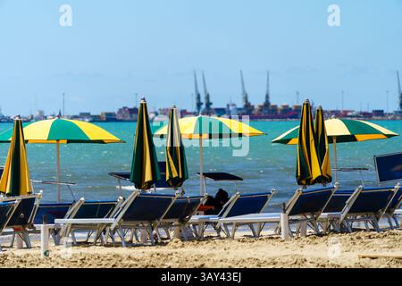 Mai 2024. Durres, Albanie. Parasols jaunes et verts et chaises longues sur la plage avec les quais derrière. Photo : © Simon Grosset Banque D'Images