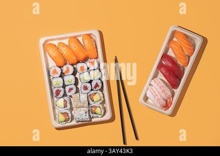 Plan minimaliste au plafond de boîtes à emporter à sushis sur fond orange, avec des rouleaux de nigiri et de maki avec un éclairage directionnel puissant Banque D'Images