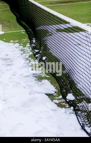 Un court de tennis est partiellement recouvert de neige, créant un contraste saisissant entre la neige blanche et l'herbe verte. Le filet divise la scène, ajoutant un Banque D'Images