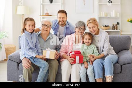 Portrait de famille heureux, trois générations de personnes, grands-parents, vieille mamie tenant un cadeau d'anniversaire Banque D'Images