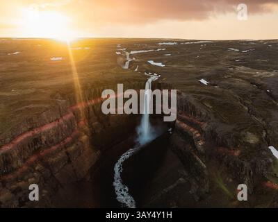 La cascade de Hengifoss plonge dans une gorge profonde, encadrée par des colonnes de basalte et des bandes d'argile rouge, capturée pendant l'heure dorée dans l'est de l'Islande. Banque D'Images