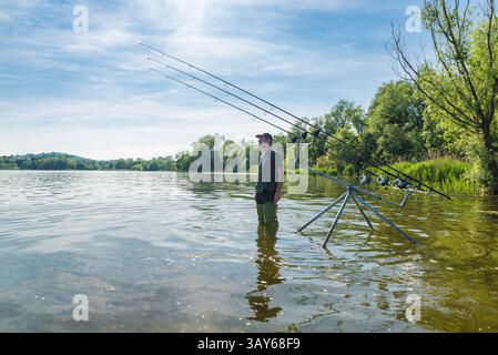 Aventures de pêche, pêche à la carpe. Homme pêchant sur un lac dans une belle journée ensoleillée. Pêcheur debout, dans l'eau avec des bottes hautes Banque D'Images