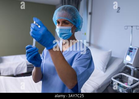 Infirmière femme mi-adulte tirant le flacon de médicament dans la seringue dans la chambre d'hôpital, avec pompe à perfusion Banque D'Images