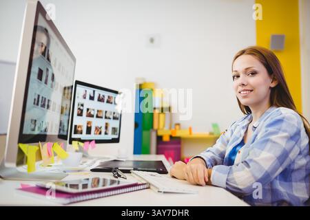 Adolescente assise au bureau à l'aide d'un ordinateur dans le bureau à domicile, avec moniteurs et tablette, espace de copie Banque D'Images