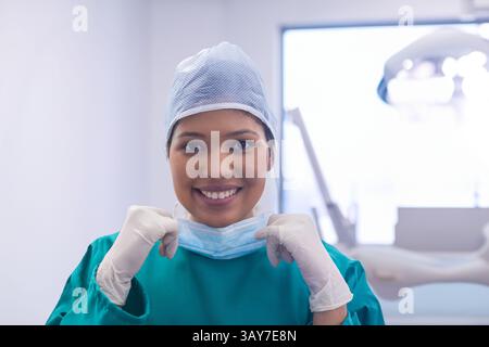 Travailleuse médicale tirant vers le bas le masque facial dans la salle de clinique, portant des gommages verts et des gants Banque D'Images